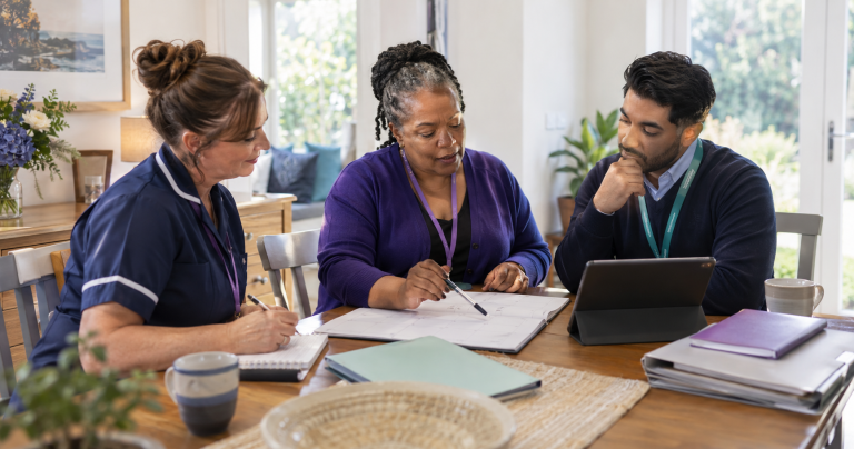 A care coordinator reviewing a shared workflow with a home-care worker and community partner.